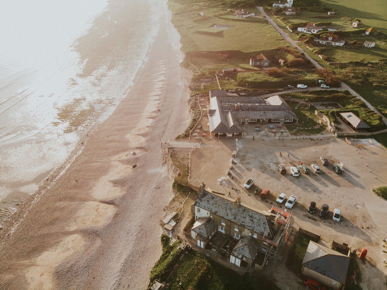 A stunning aerial view of a coastal village with a sunlit beach and parked cars at sunset.