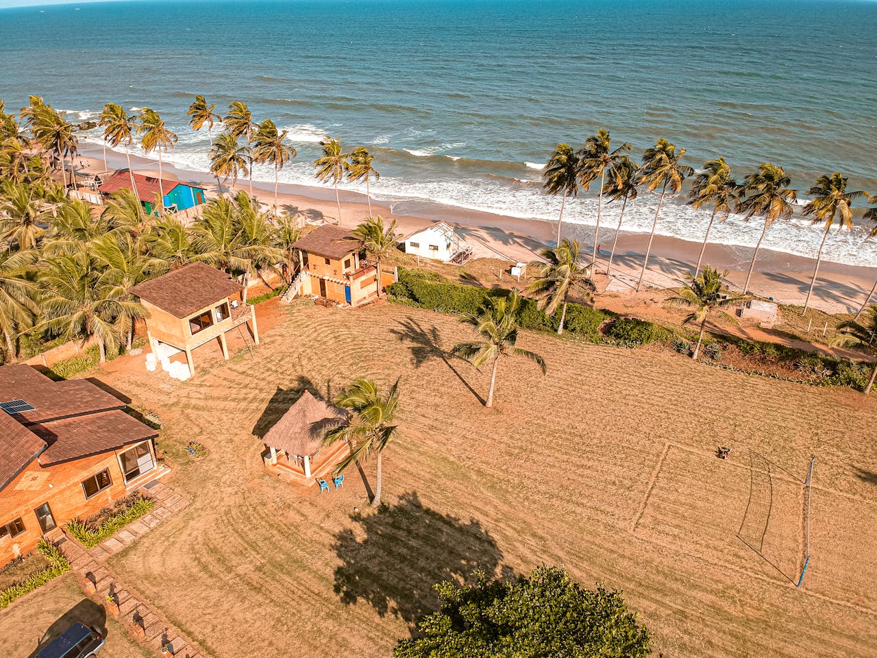 A scenic aerial view of beachfront homes surrounded by palm trees and the ocean's waves on a sunny day.